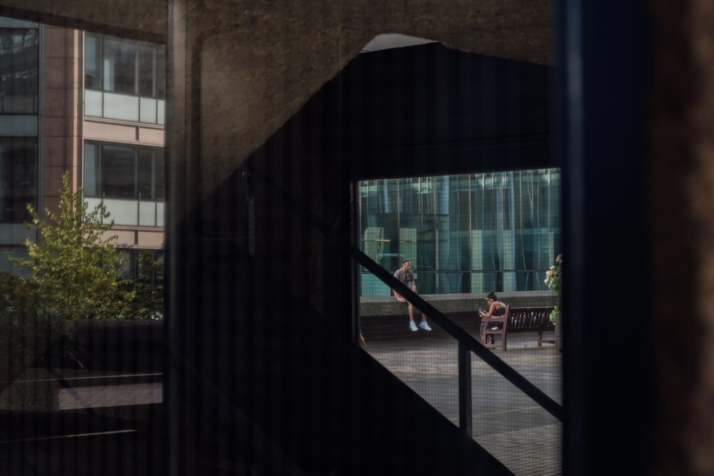 Una vista de una persona sentada en un banco a través de una ventana