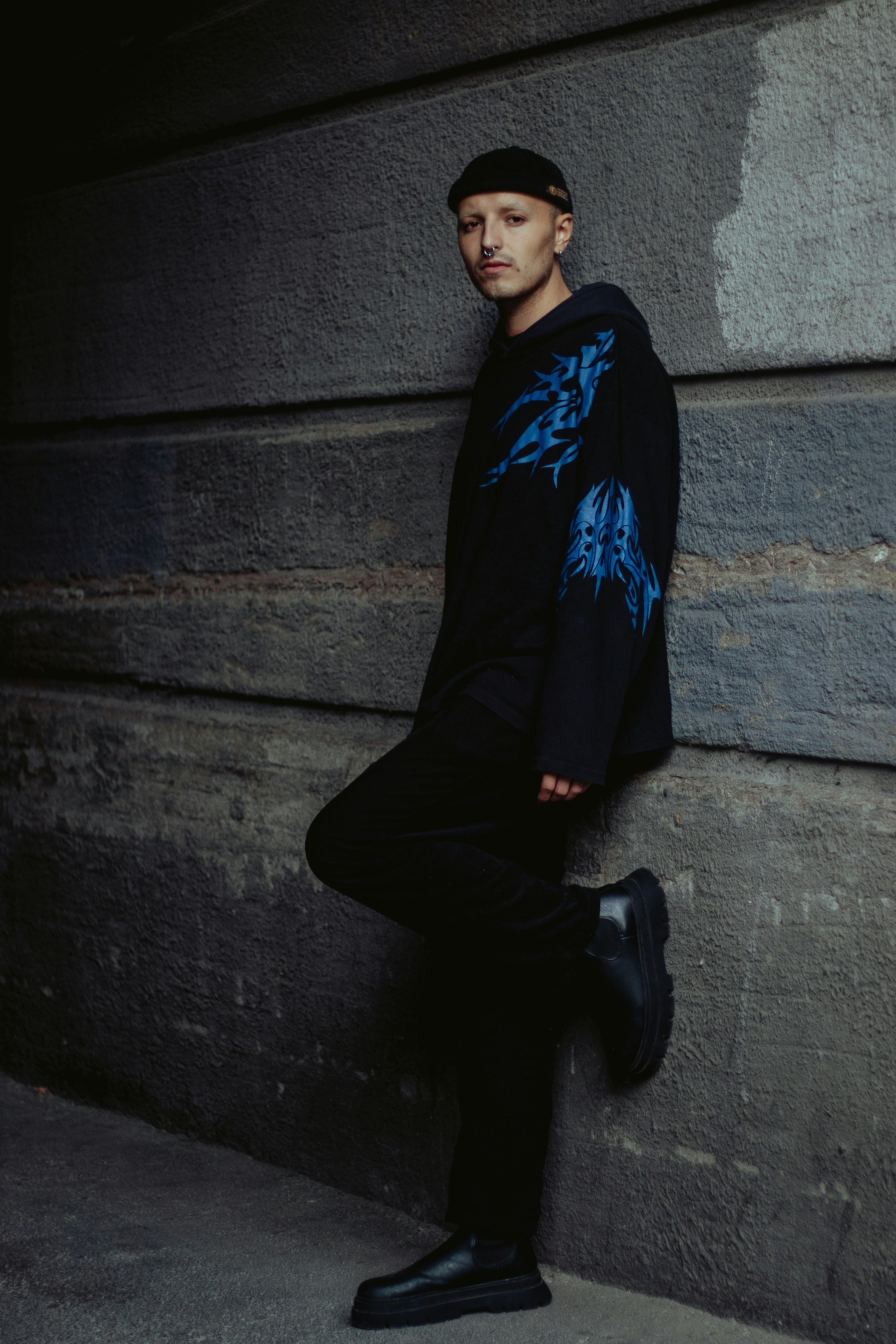 Plain black oversized tee hanging against concrete wall, underground aesthetic dim lighting