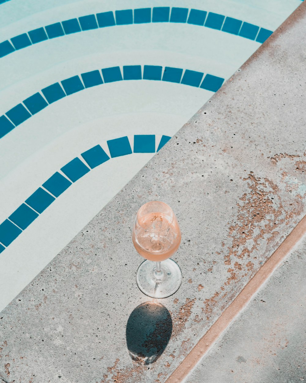 a glass of wine sitting next to a swimming pool