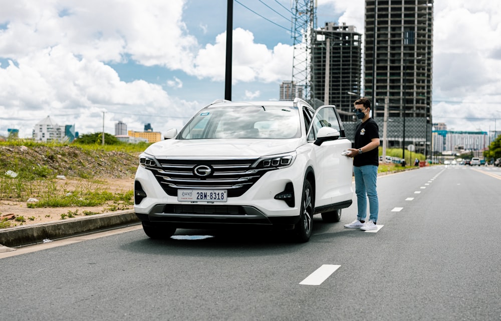 a man standing next to a white car on the side of a road