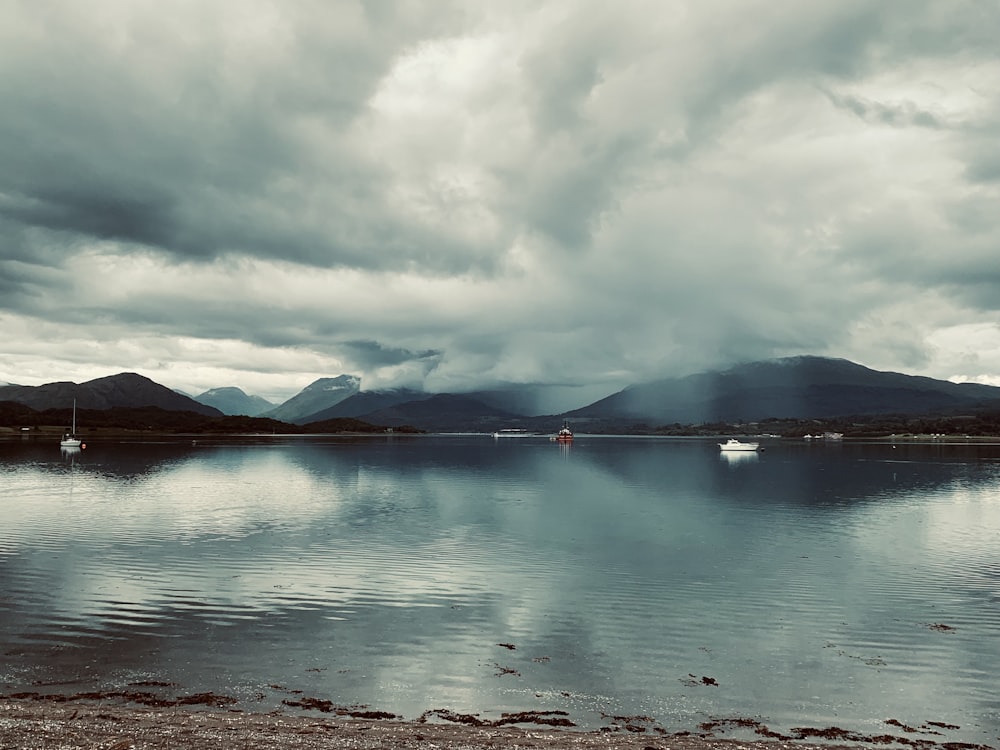 a body of water surrounded by mountains under a cloudy sky