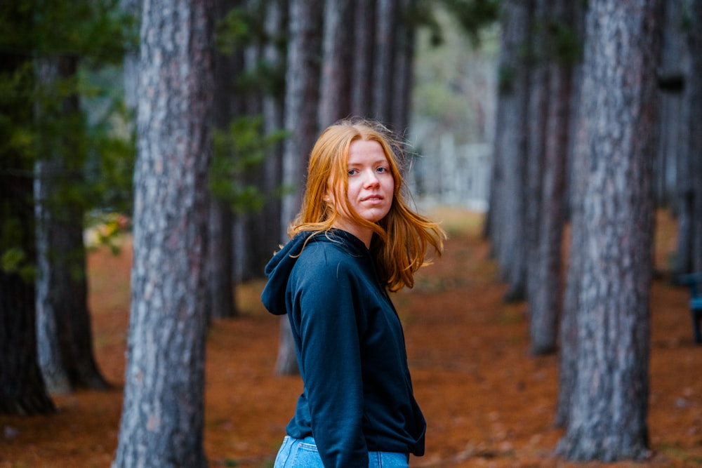 a woman standing in a forest with trees in the background