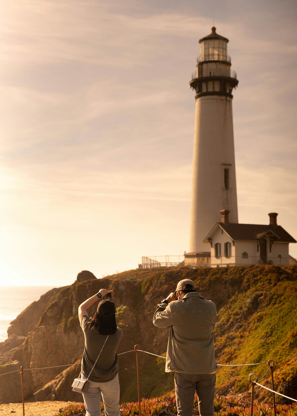 a couple of people standing next to a light house