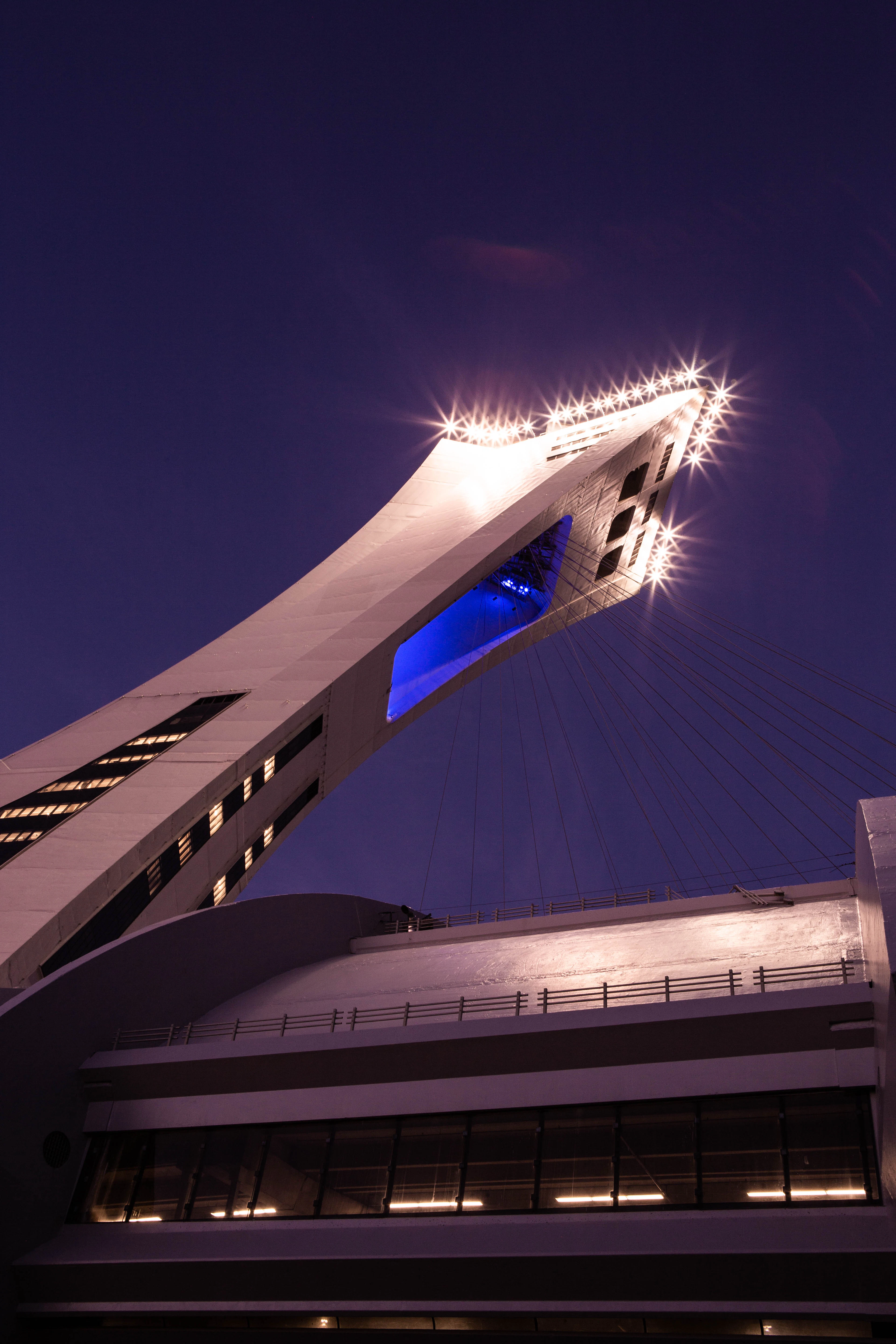 The inclined tower of Olympic Stadium is lit white against a deep blue dusk sky.