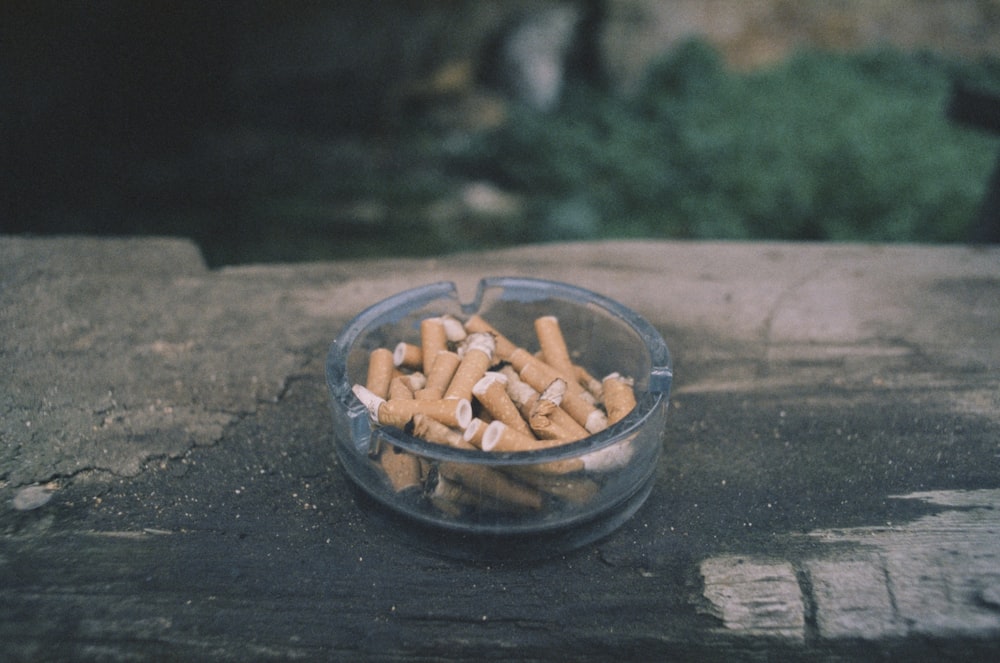 Un tazón de vidrio lleno de cigarrillos sentado encima de una mesa de madera