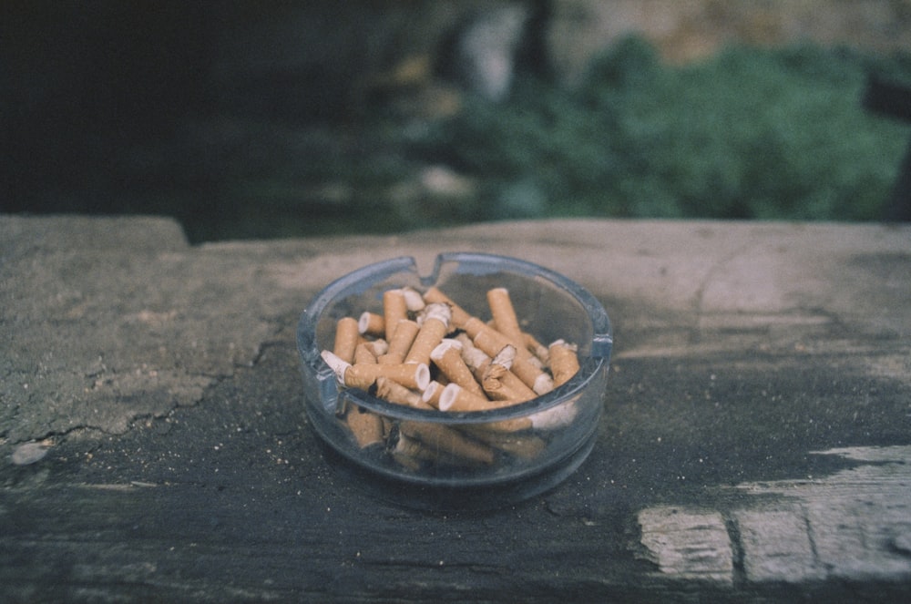 a glass bowl filled with cigarettes sitting on top of a wooden table