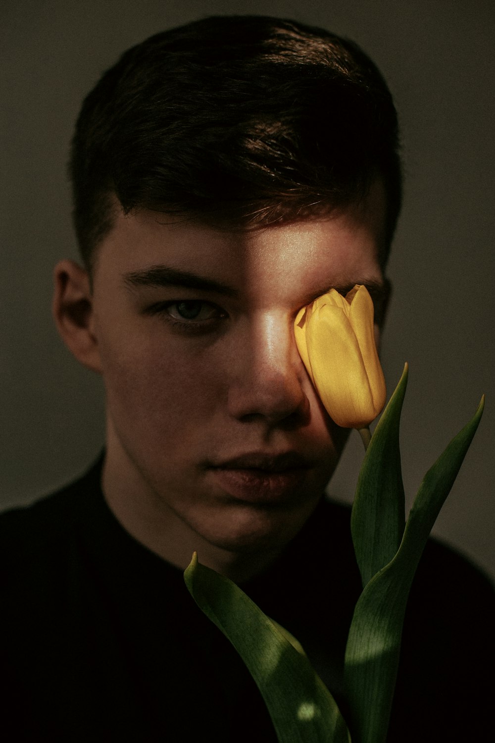 a young man holding a yellow flower in front of his face