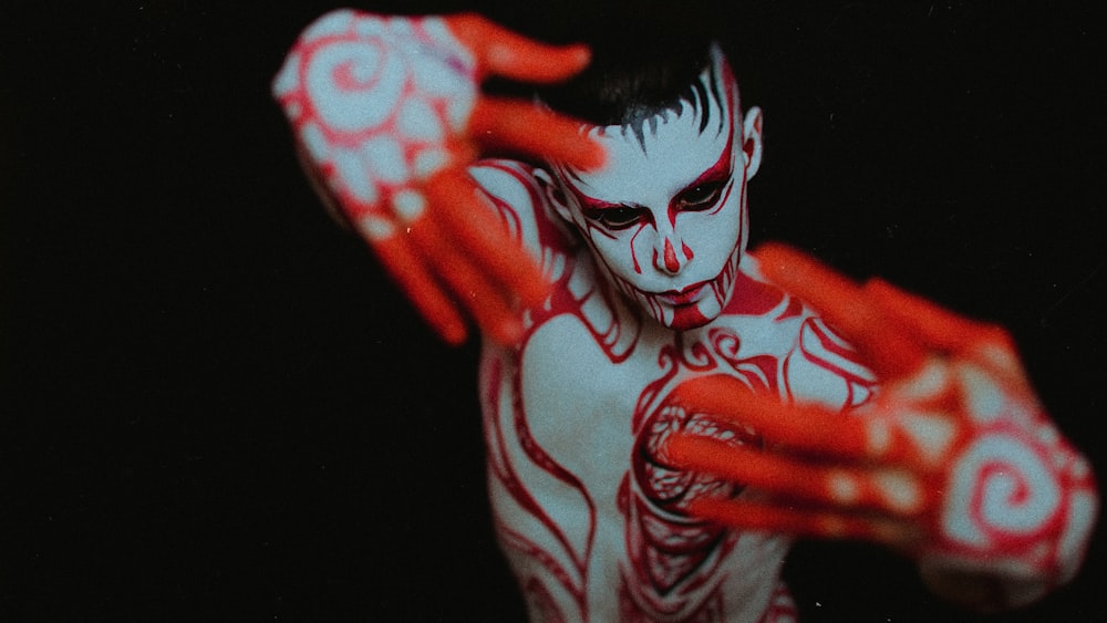 a man with white and red body paint holding his hands up