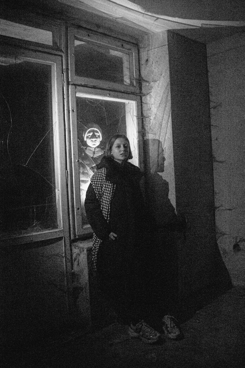 a black and white photo of a woman standing in front of a window