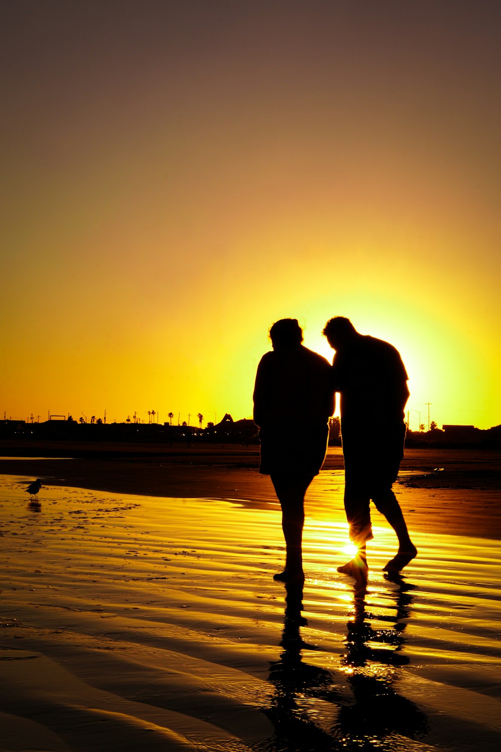 two people walking on a beach at sunset
