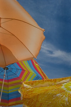 Two colorful beach umbrellas side by side on a lively shoreline.
