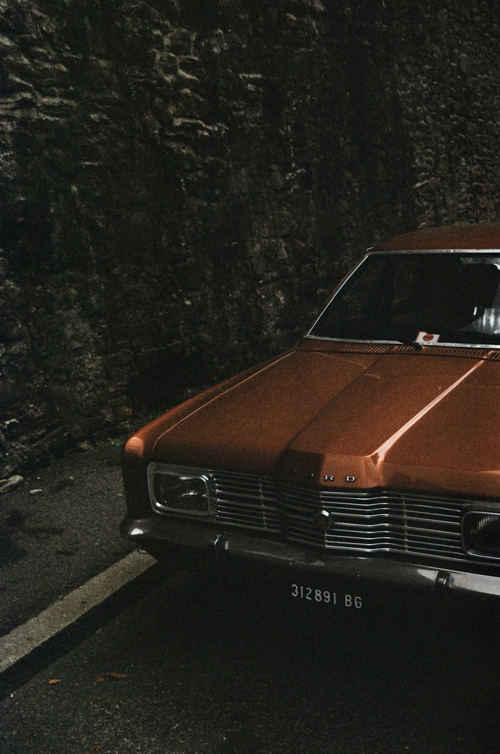 a brown car parked in front of a stone wall