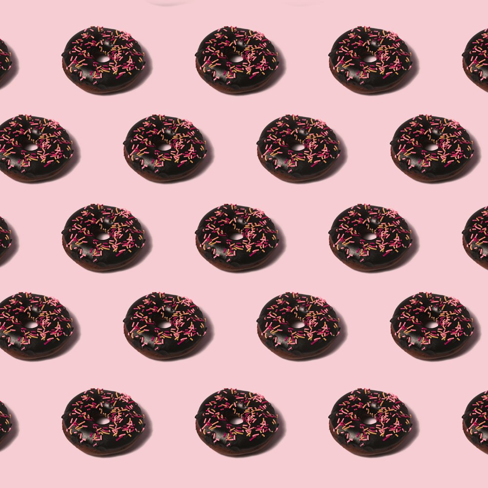 a group of donuts with pink sprinkles on a pink background