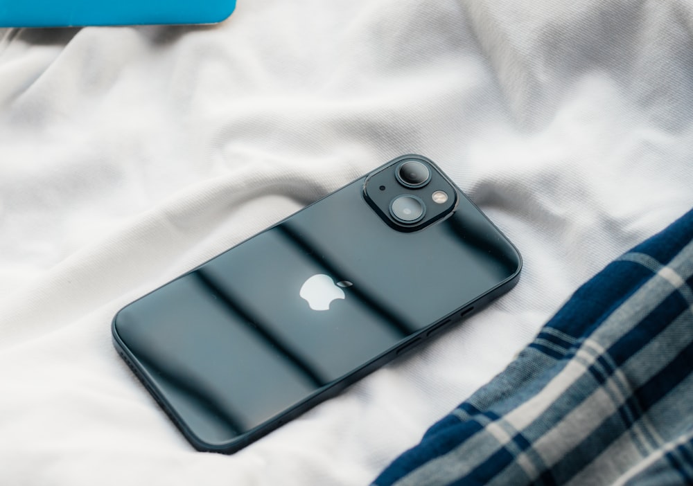 a black iphone sitting on top of a bed