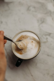 Close-up of a hand stirring Java Burn powder into a steaming cup of coffee.