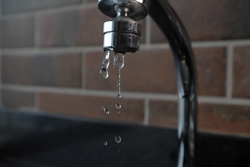 Close-up of a dripping tap against an exposed-brick industrial wall