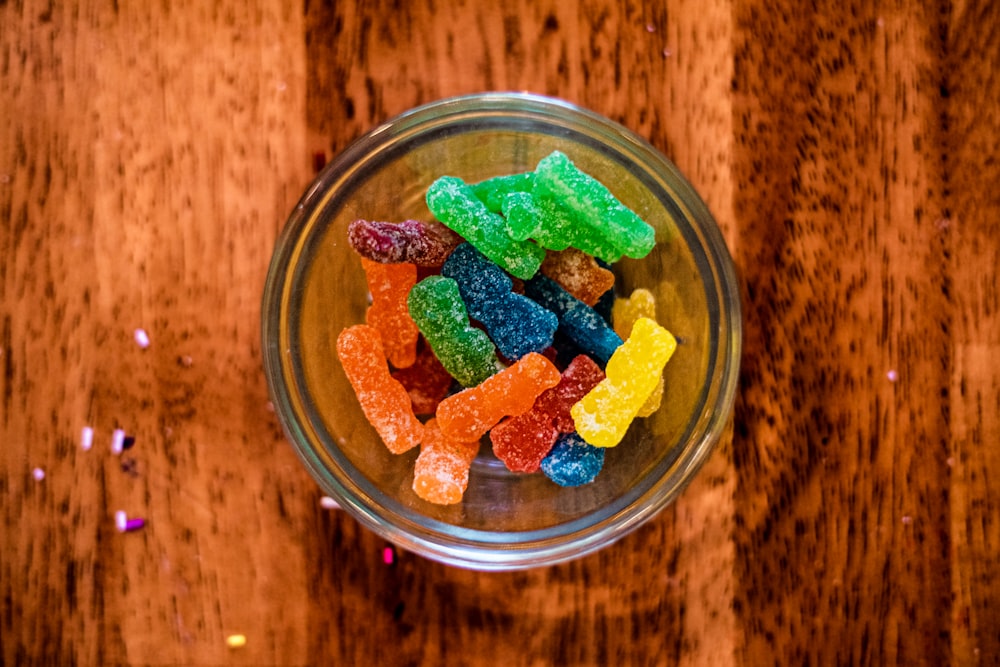 a glass bowl filled with gummy bears on top of a wooden table