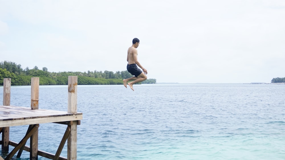 um homem pulando de uma doca no oceano