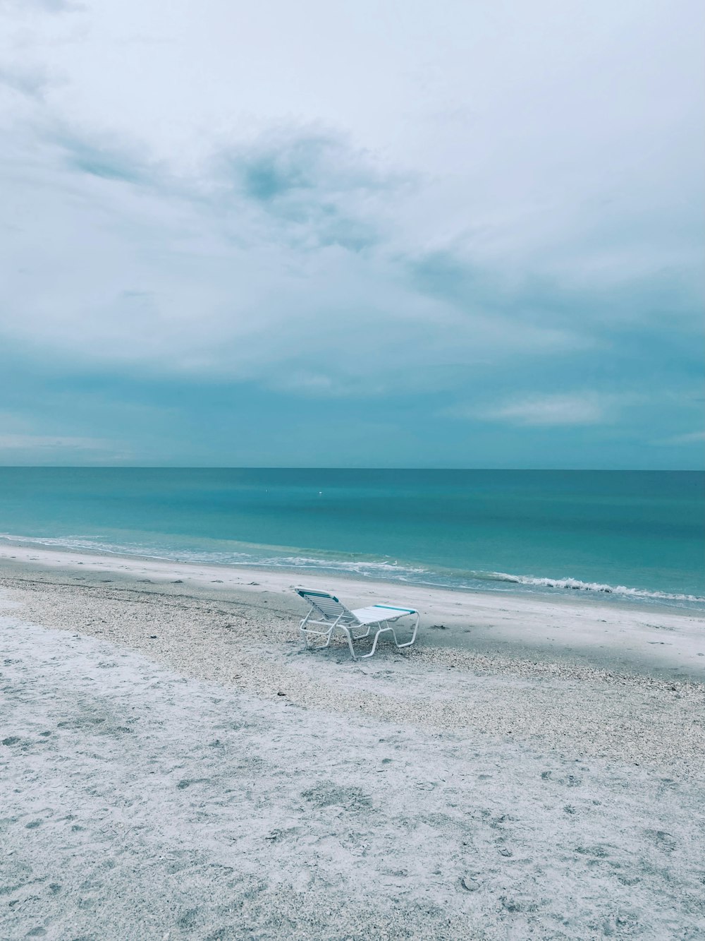 a white lawn chair sitting on top of a sandy beach