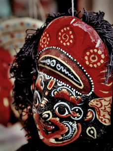 Close-up of hands painting a vibrant carnival mask with red, black, white, and gold details.