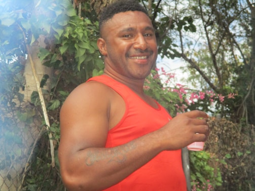 A smiling person enjoying a green smoothie outdoors surrounded by nature.