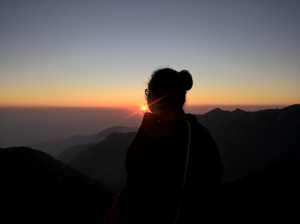 a woman standing on top of a mountain at sunset