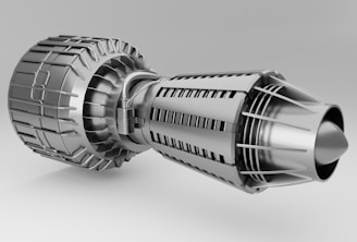 A detailed and intricate metallic structure resembling a jet engine or turbine, featuring various components like fins, vents, and a cylindrical body. The surface has a polished, silver appearance, highlighting the precision of its engineering.