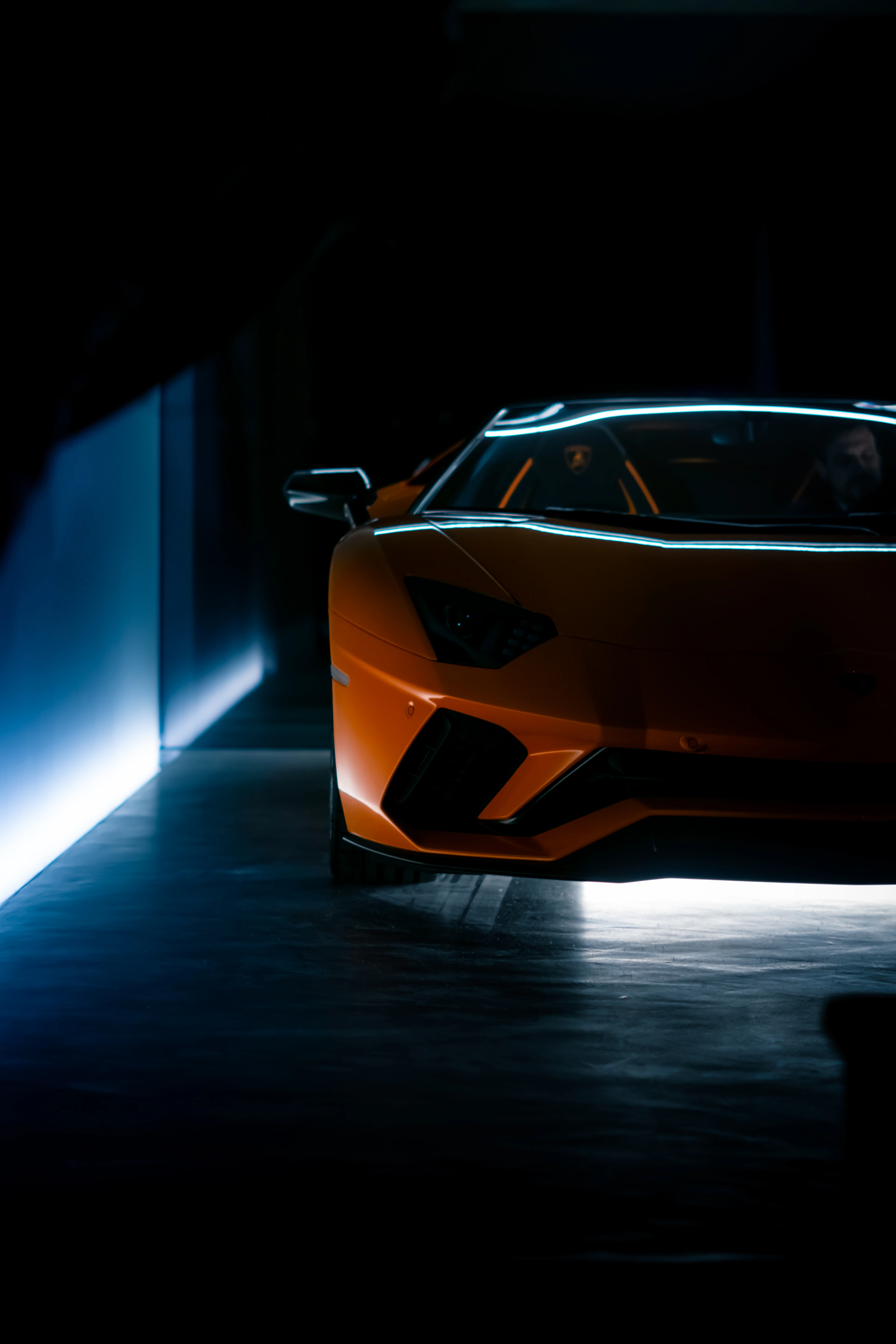 Orange supercar in a dark studio revealed by a moving spotlight