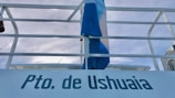 A railing with a flag in blue and white colors is visible against a cloudy sky. The text 'Pto. de Ushuaia' is prominently displayed.