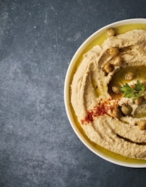 a white bowl filled with hummus and olives