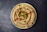 A beautifully presented plate of creamy hummus garnished with whole chickpeas, olive oil, a sprig of parsley, and a sprinkle of paprika. The hummus is arranged in a swirl pattern, with the topping centrally located, enhancing the visual appeal.