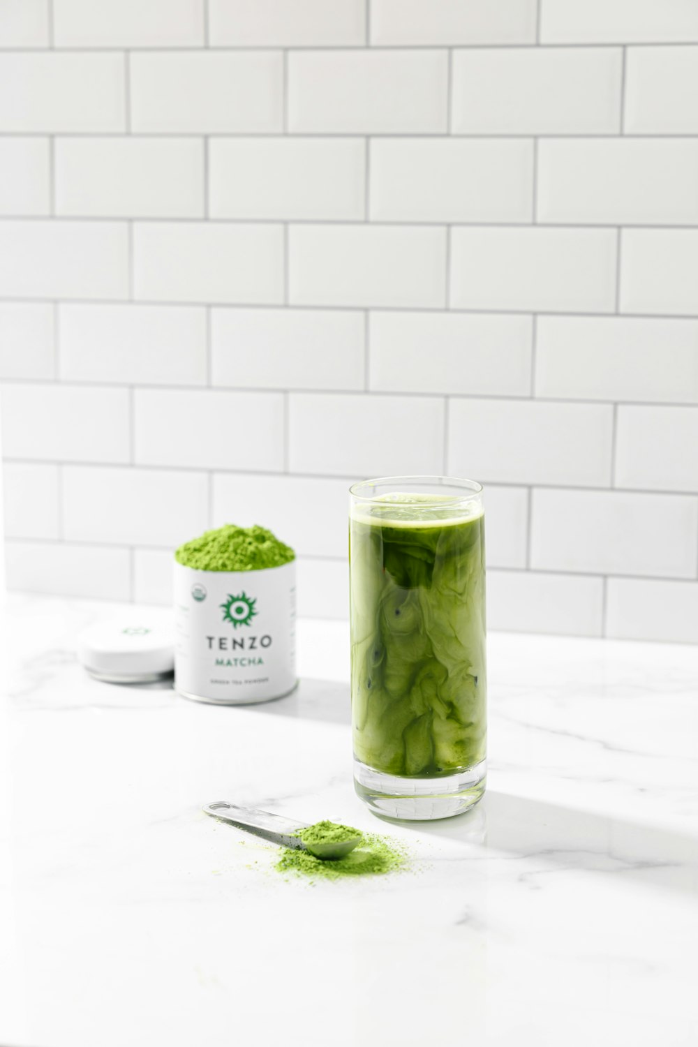 a glass filled with green liquid next to a can of green tea