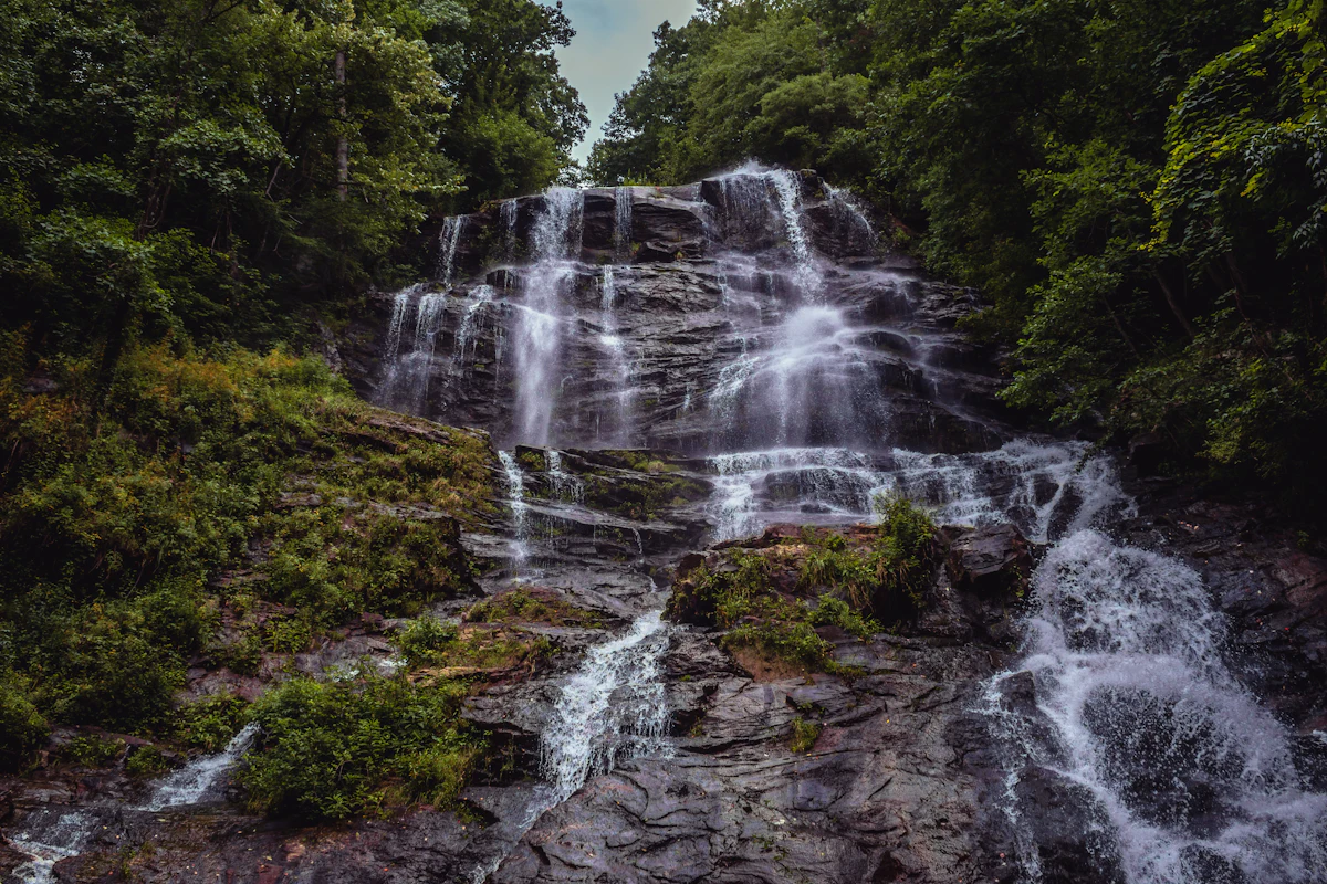 Amicalola Falls spilling down a wide rock face between green summer woods