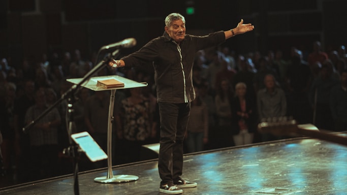 Mark Dolan confidently hosting a lively corporate event on stage with a microphone in hand.