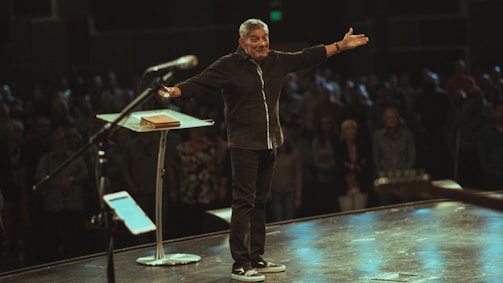 A warm photo of a man speaking passionately on stage, smiling with confidence and hope.