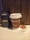A handheld radio is placed beside a brown disposable coffee cup on a counter. The coffee cup has a white lid and features 'COFFEEHOLIC' printed in large letters. A white napkin with a 'deli2go' logo is neatly folded next to the cup. The background consists of wooden paneling.