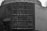 A black and white image of a public clock plaque with inscriptions in Portuguese. The text includes 'Relógio Público de Nichile' and mentions a specific inauguration date, as well as names and titles.