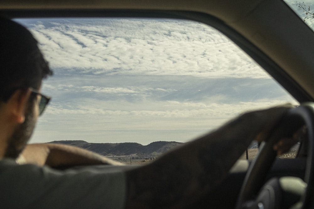 a man driving a car with mountains in the background