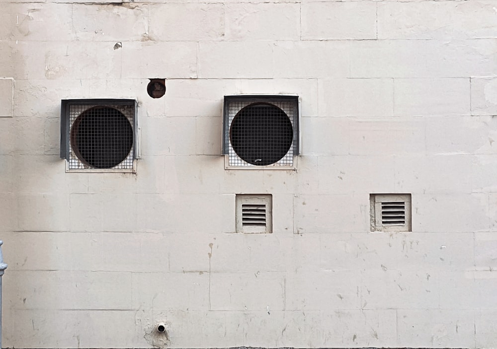 a white wall with three round windows and a blue fire hydrant