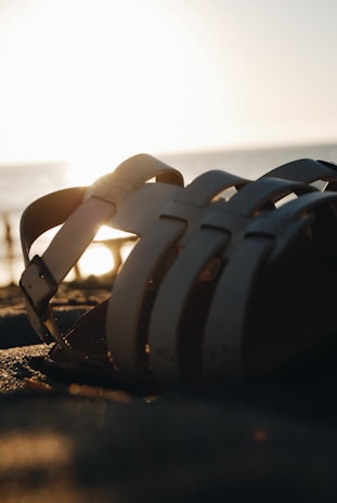A casual sandal set against a backdrop of soft sand on a beach at sunset.