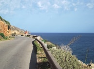 A VIP van cruising along a coastal road with the sparkling Aegean Sea on one side and rugged cliffs on the other.