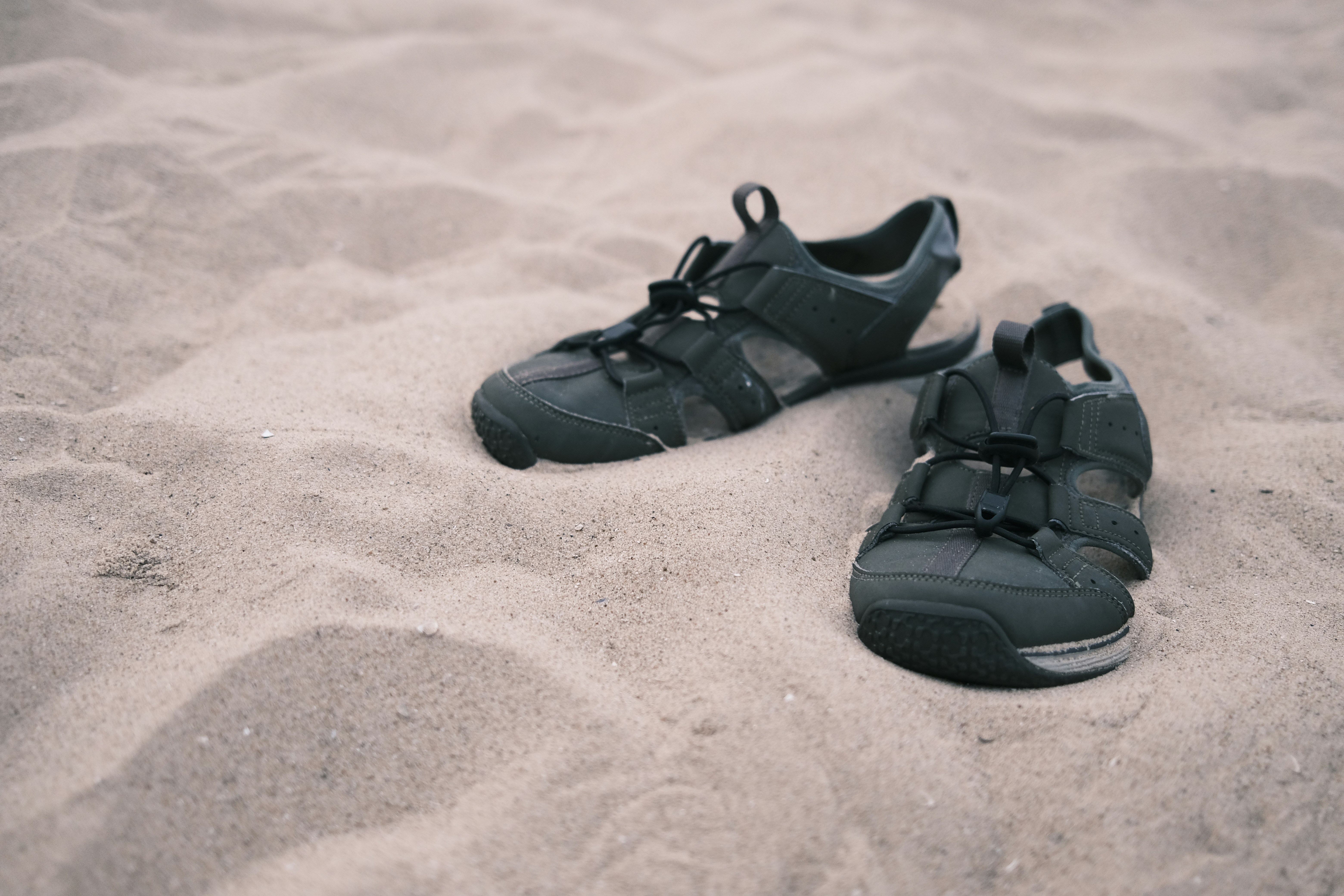 a pair of black shoes sitting on top of a sandy beach
