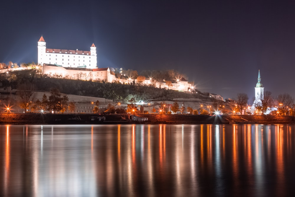 a castle is lit up on a hill above the water