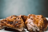 Close-up view of roasted chicken pieces on a white plate. The chicken is cooked with a golden-brown crispy skin, suggesting it is well-seasoned and flavorful.