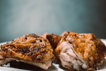 Close-up view of roasted chicken pieces on a white plate. The chicken is cooked with a golden-brown crispy skin, suggesting it is well-seasoned and flavorful.