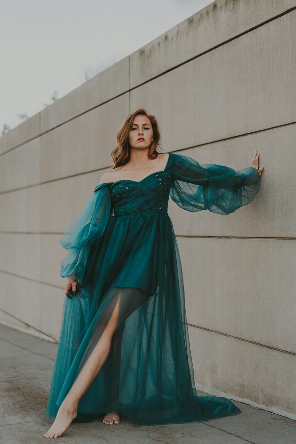 a woman in a green dress leaning against a wall