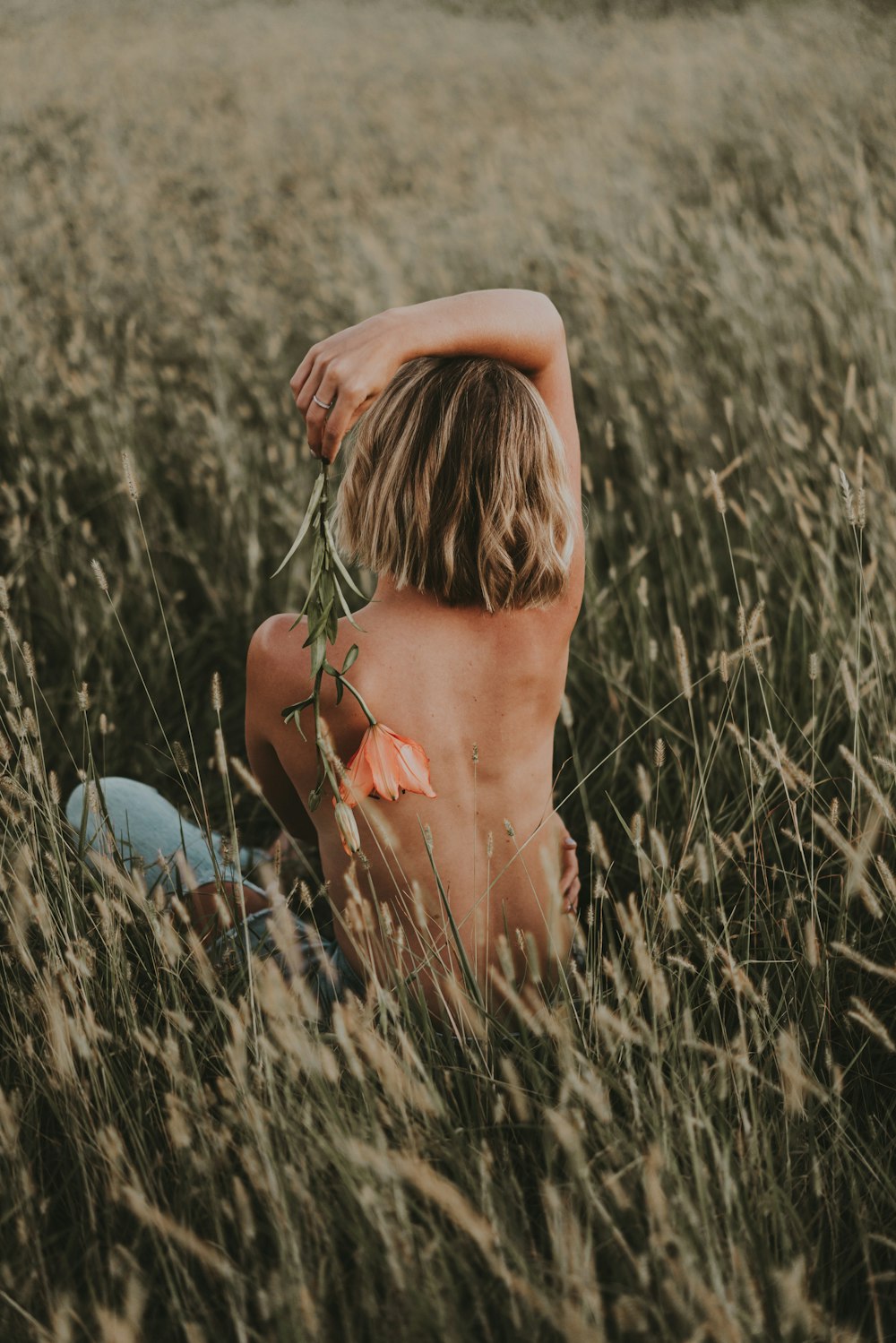 a naked boy sitting in a field of tall grass