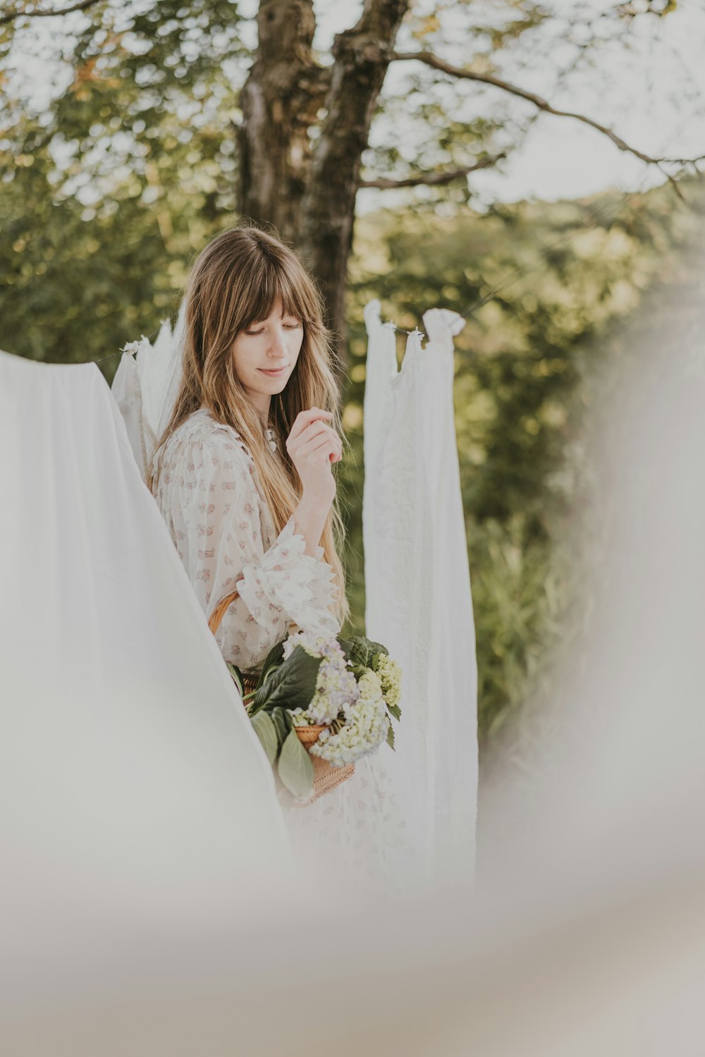 a woman standing next to a tree holding a bouquet of flowers