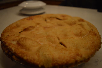 A close-up shot of a hand holding a steaming, freshly baked pie with golden crust.