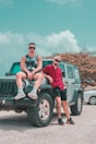 two men sitting on the back of a green jeep